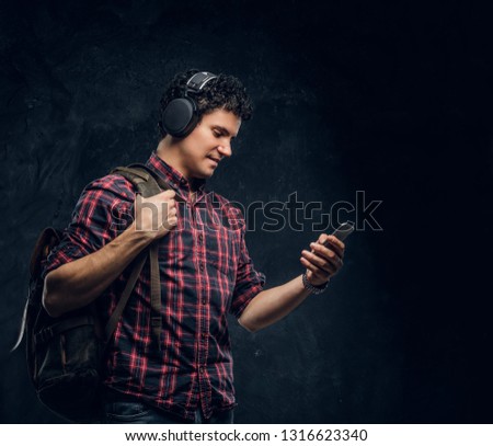 Young guy in wireless headphones listens to music and using the smartphone in a studio against the background of the dark wall