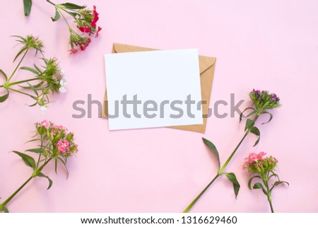  Top view of envelope and blank greeting card with flowers on pink background.