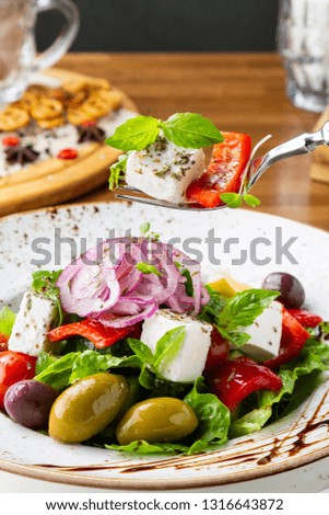 Greek salad with feta cheese, olives and herbs, served in a white plate on a table in a restaurant