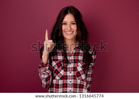 Picture of smiling handsome woman showing up by her finger isolated over the pink background.