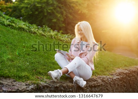 Smiling handsome woman listening relaxing music In the headphones  with her mobile phone or tablet at the park. A student listens to an online lecture and prepares for exams. girl enjoying loneliness