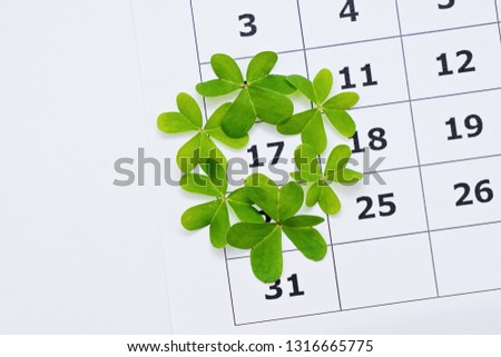 Above view of paper calendar sheet with selected date March 17 in frame from clover leaves