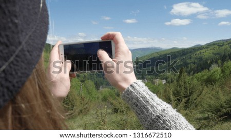 A woman is taking pictures against the background of big mountains and the green mountain river. on the phone. selfie or self-portrait on a smartphone. Enjoys adventure and travel concept