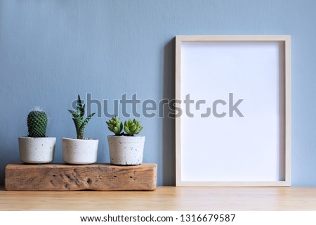 Minimalistic room interior with mock up photo frame on the brown wooden table with beautiful cacti in design hipster white pot. Grey walls. Stylish and floral concept of mock up poster frame. 