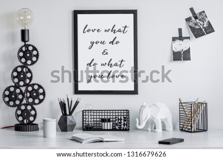 Modern and stylish black and white home decor mock up. Creative desk with blank picture frame or poster, desk objects, office supplies, elephant figure and design table lamp on a white background.