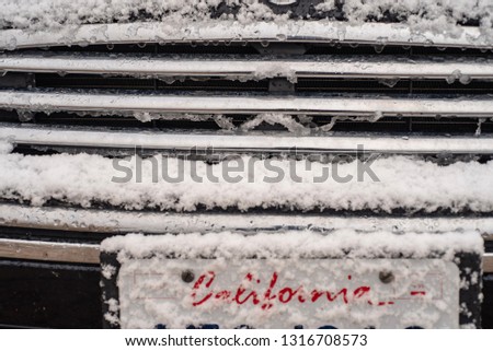 red lettering script word spells California under new fallen snow on a car license plate  front of car in winter in California