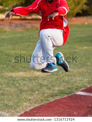 An african american triple jumper is in phase three of the hop, skip and jump during track and field practice outdoors in the winter. Royalty-Free Stock Photo #1316711924