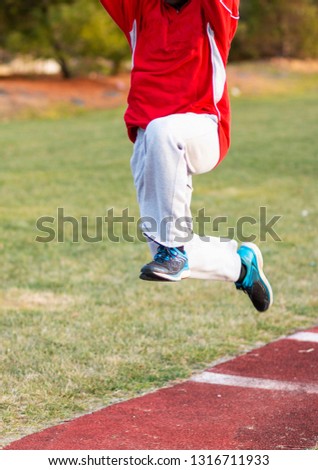 An african american high school boy is practicing the hop, skip and jump phases of the triple jump at track and field practice ouside in the winter. Royalty-Free Stock Photo #1316711933