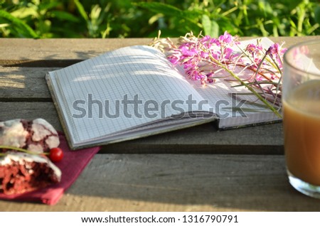 An open notebook with a blank sheet with purple summer wildflowers. summer morning, diary, inspiration. and pink flowers on wooden table top view in flat lay style. Woman working desk.