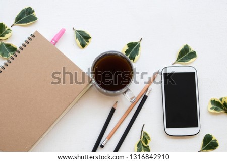 notebook planner ,mobile phone for business work with hot coffee and leaf arrangement flat lay style at office desk