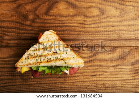Delicious sandwich stacked high with a juicy ham , cheese, fresh lettuce, onion and tomato on a fresh bun with  standing on  wooden table