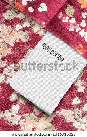 Clothes label says 100% cotton on red floral textile background
