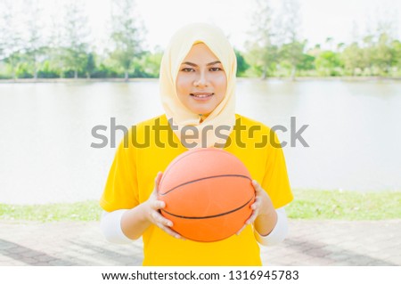 Young female wearing hijab play basketball in park