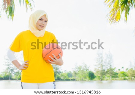 Young female wearing hijab play basketball in park