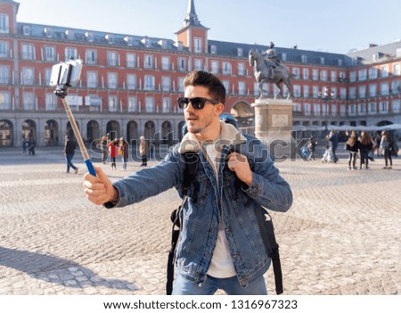 Attractive young caucasian tourist student man having fun happy and excited taking a selfie with smart mobile phone in Plaza Mayor, Madrid, Spain. Travel,vacation, holidays around Europe concept.