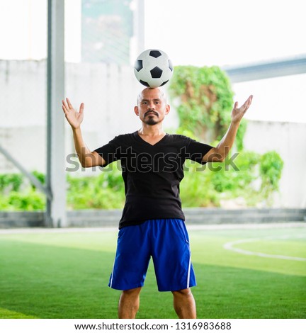 portrait of a male football player juggling a ball on his head on green artificial turf