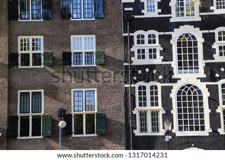 detailed filled frame background wallpaper shot of a typical facade made of brown and black bricks with large white rectangular windows of old narrow dutch canal houses. Amsterdam, Netherlands