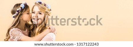 adorable daughter kissing and hugging beautiful mother on yellow background