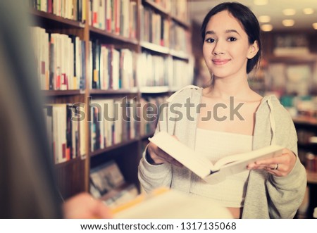 Cheerful girl reading interesting book in bookshop