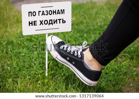 Teenagers foot over green grass near small white banner with Russian text: Do not walk on the lawns!