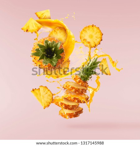 Flying in air fresh ripe whole and cut baby Pineapple with juice splash isolated on pastel pink background. High resolution image