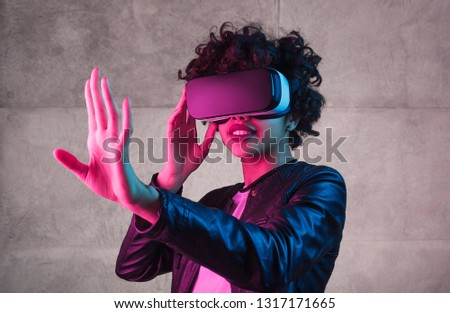 Lovely African American teen girl trying to interact with virtual reality while standing near concrete wall under bright light Royalty-Free Stock Photo #1317171665