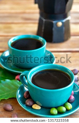 Cup with black coffee served outside with raw green, mature red and roasted coffee beans, decorated with green leaves from coffee plant close up