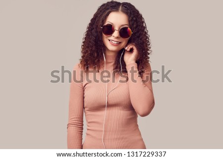 Fashion portrait of bright gorgeous positive girl with curly hair listening music on headphones in studio