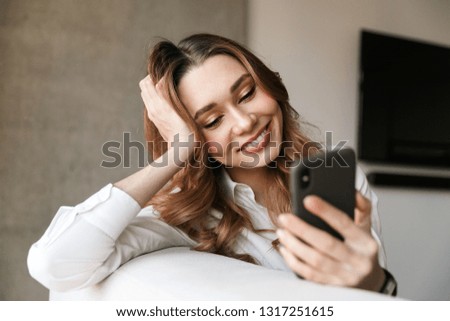 Photo of beautiful young business woman dressed in formal clothes shirt indoors using mobile phone.