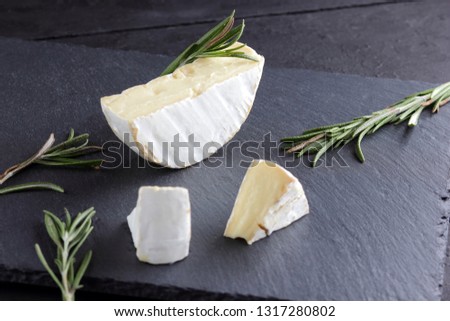 Camembert and rosemary on black stone board. Soft cheese with white mold on black background. Sliced cheese and rosemary branches on slate board