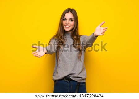 Young woman over yellow wall presenting and inviting to come with hand