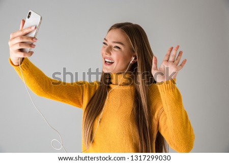 Image of a beautiful happy young woman isolated over grey wall background using mobile phone talking waving.