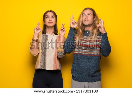 Hippie couple over yellow background with fingers crossing and wishing the best