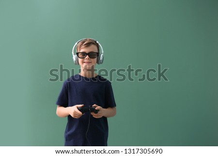 Cute boy playing video game on color background