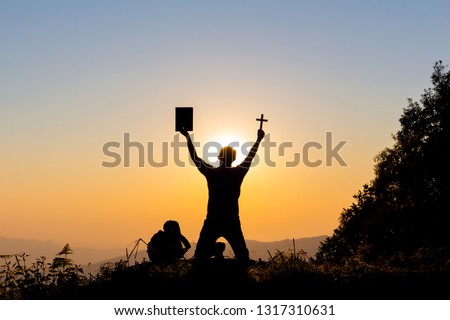 human praying to the GOD while holding a crucifix symbol with bright sunbeam on mountain at sunset time