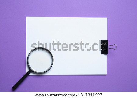 Blank sheets of paper with clip and magnifying glass on color background