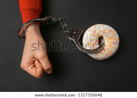 Woman handcuffed to tasty doughnut on dark background. Concept of addiction Royalty-Free Stock Photo #1317350648