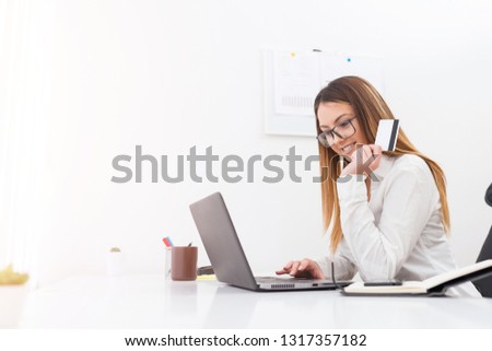 Attractive young businesswoman holding a bank card while shopping on a notebook in her office.