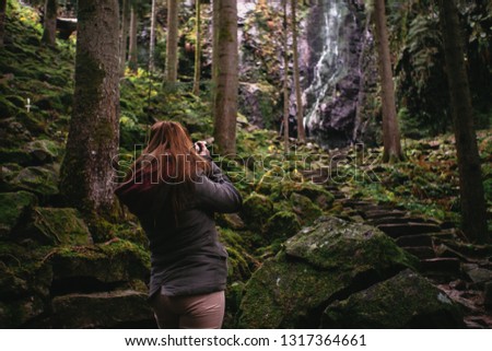 Young woman taking a picture of a waterfall in the forest