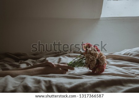 A close up of hands holding plastic flowers on a bed. With a soft edit.