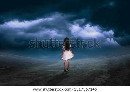 The little girl walked on the way on a day with a dark sky and rain.