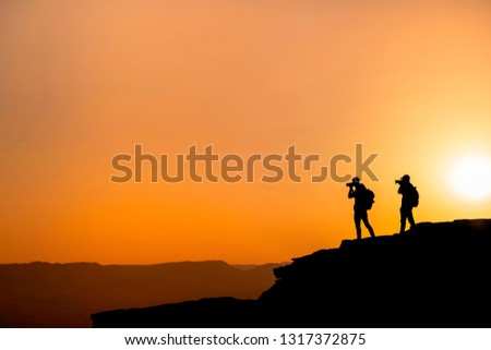 Silhouette of a unrecognizable photographers who shoots a sunset in the mountains. Photographer concept