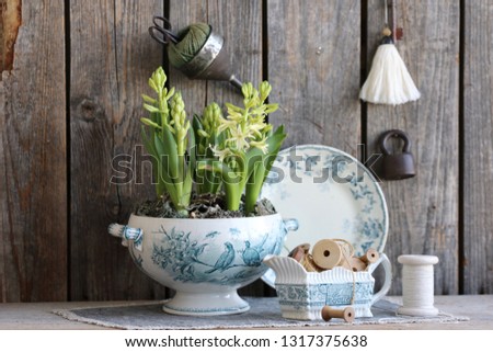 Spring scene with hyacinth in antique old tureen, bird decor transfer, quail eggs in natural grass nest, gravy boat, spool, vintage industrial funnel, rustic scissors, padlock, keys on wood background