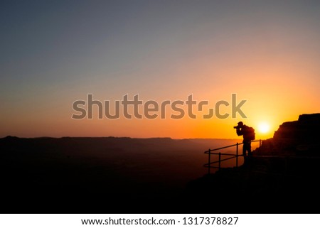Silhouette of a unrecognizable photographer who shoots a sunset in the mountains. Photographer concept