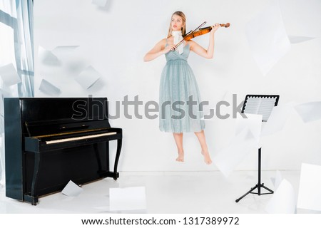 floating girl in blue dress playing violin near piano with sheets of paper in air 