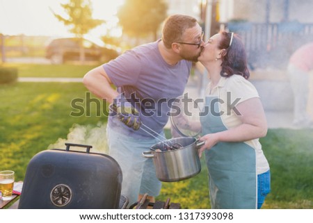 Picture of middle age couple making barbeque and kissing in their backyard. Family lunch on summer day.