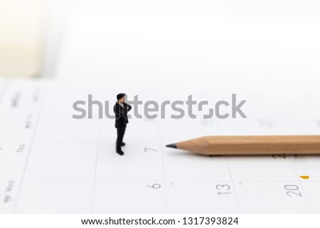 Miniature people : Businessman standing on the calendar to set the date for the meeting . Image use for business meetings concept.