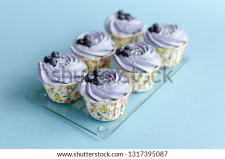 Set of lemon cupcakes decorated with fresh blueberries on glass board on blue background