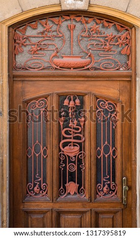 Wooden door with glass fillings and beautifully wrought grilles. An old iron wrought-iron grille of the entrance door.