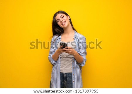 Teenager girl over yellow wall sending a message with the mobile